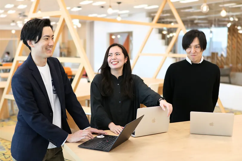 Three people standing at a table, laptops open