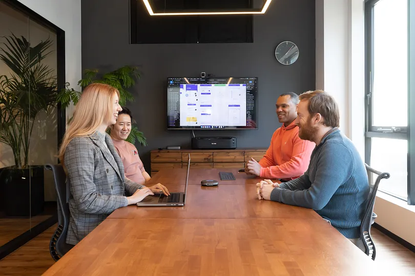 Four people sitting around a conference table, one with a laptop open