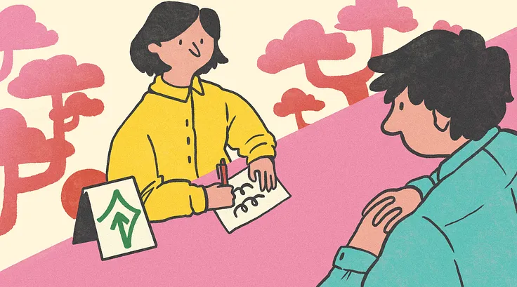 A person at a desk with the help mark on it accommodates a hearing impaired person by writing instead of speaking.