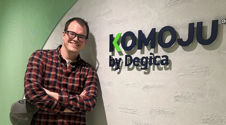 Richard standing next to a KOMOJU by Degica sign.