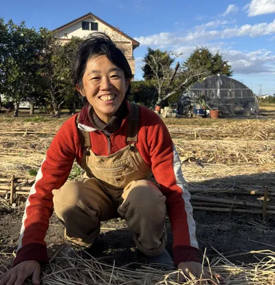 Ayako crouching in a straw-covered field.